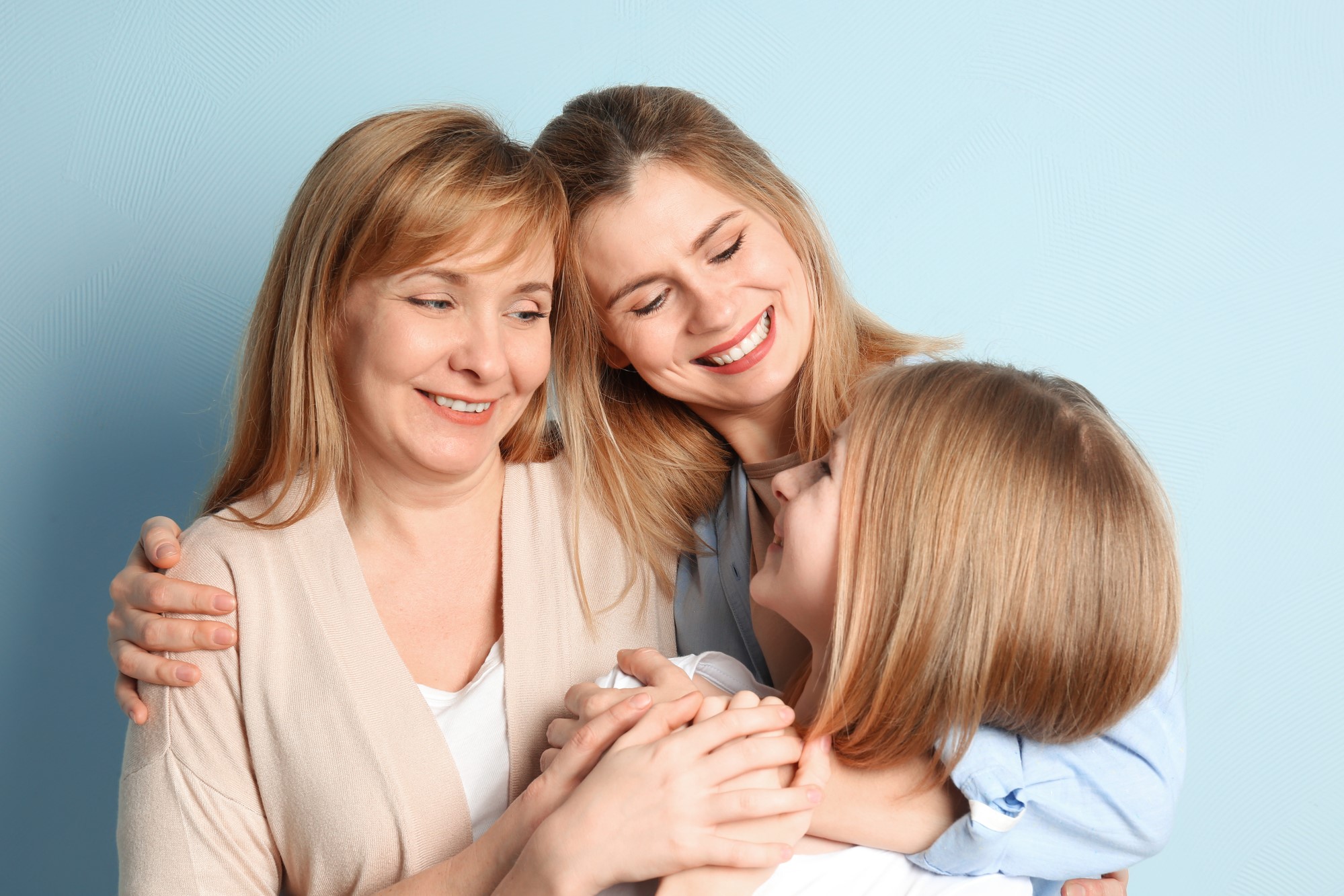 Happy young woman with her mother and daughter on color background